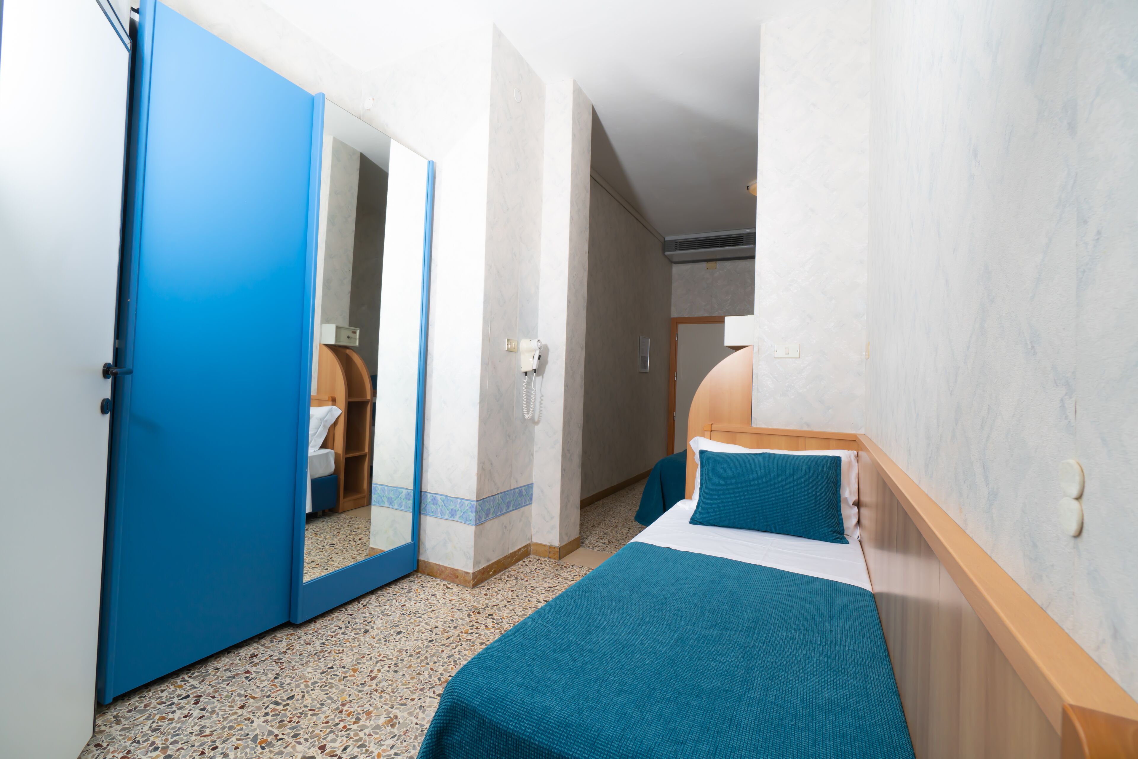 Un dormitorio con una cama, una puerta azul y un espejo.