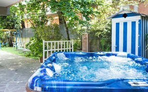 A hot tub in a backyard with a swing set and a blue and white shed in the background. - Hotel Sampaoli (Bellaria-Igea Marina)