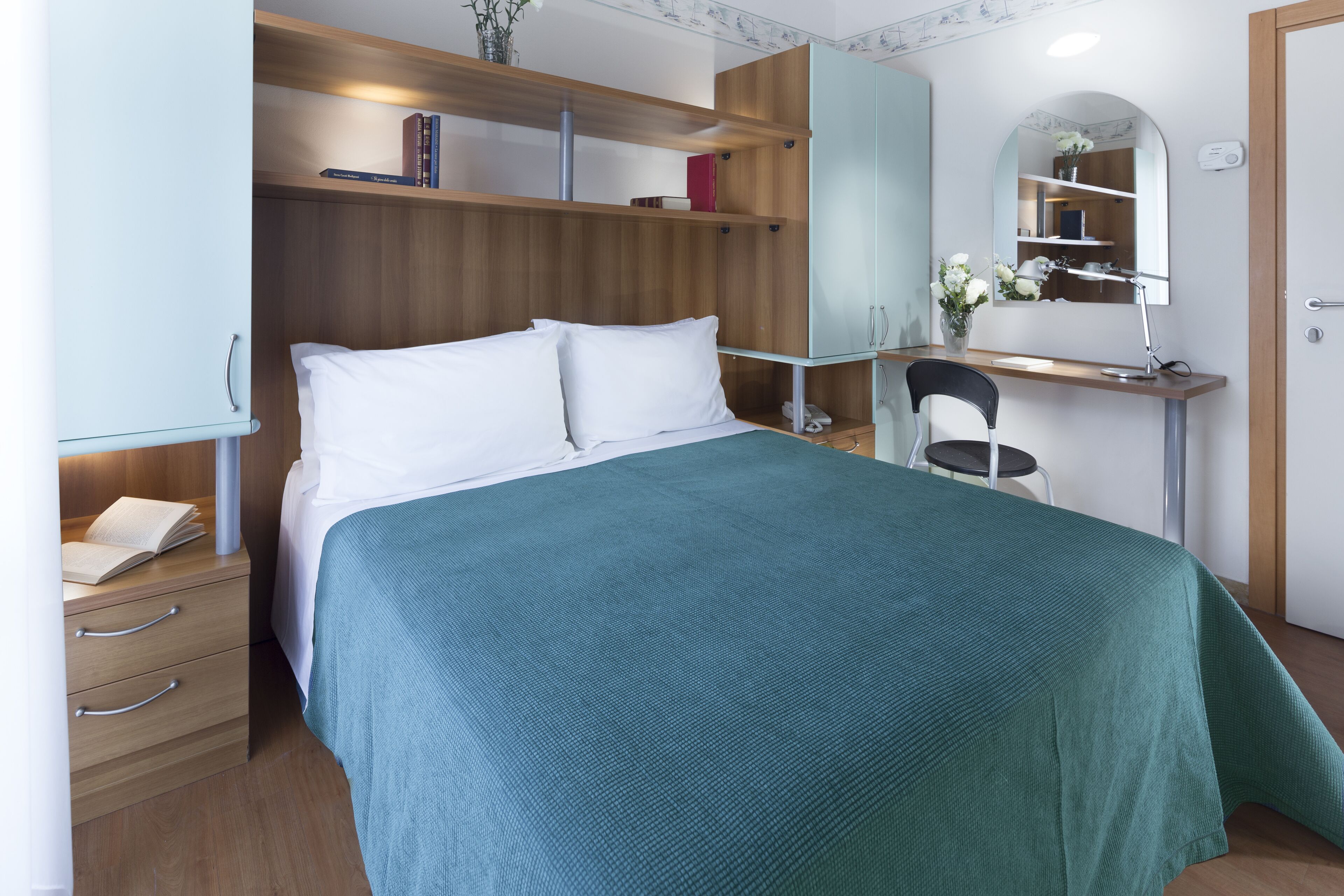 Una camera da letto con un letto, una scrivania con sedia, un armadio e uno specchio.