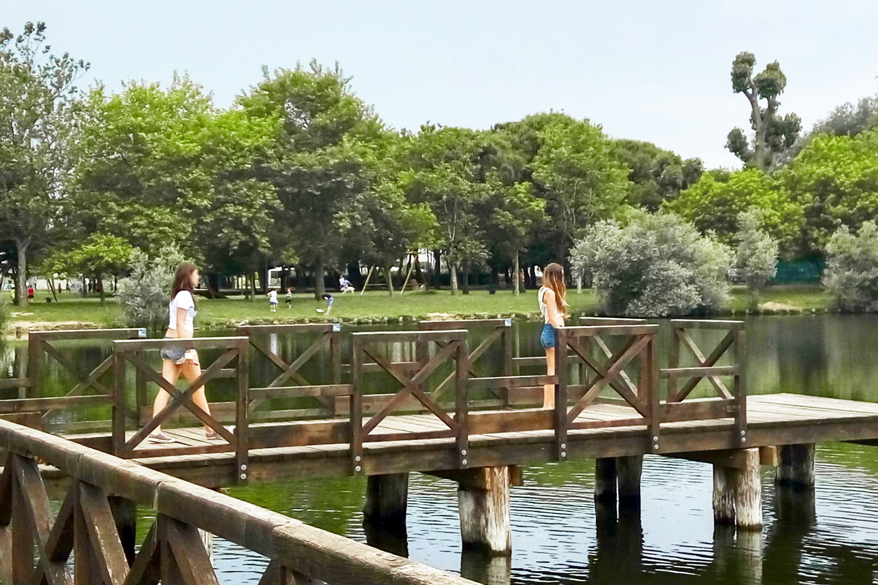 A wooden bridge over a calm body of water with lush greenery in the background.