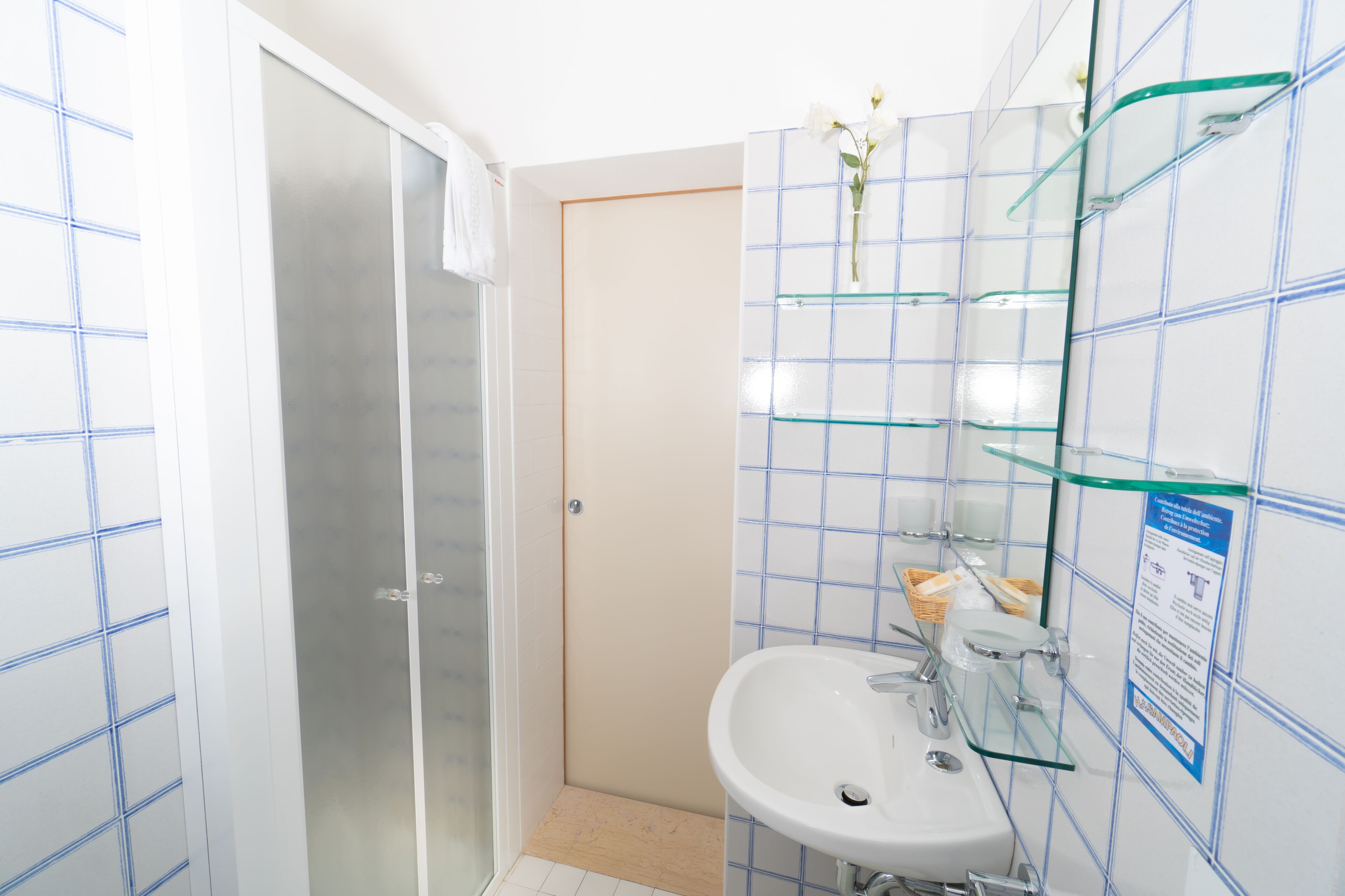 Een badkamer met een glazen douchecabine, een wit wastafeltje en een betegelde muur met blauwe accenten.