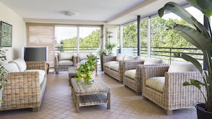 A sunlit room with wicker furniture, large windows, and potted plants. - Hotel Sampaoli (Bellaria-Igea Marina)