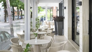 A cafe with round tables and wicker chairs, outdoor seating, and a view of the street. - Hotel Sampaoli (Bellaria-Igea Marina)