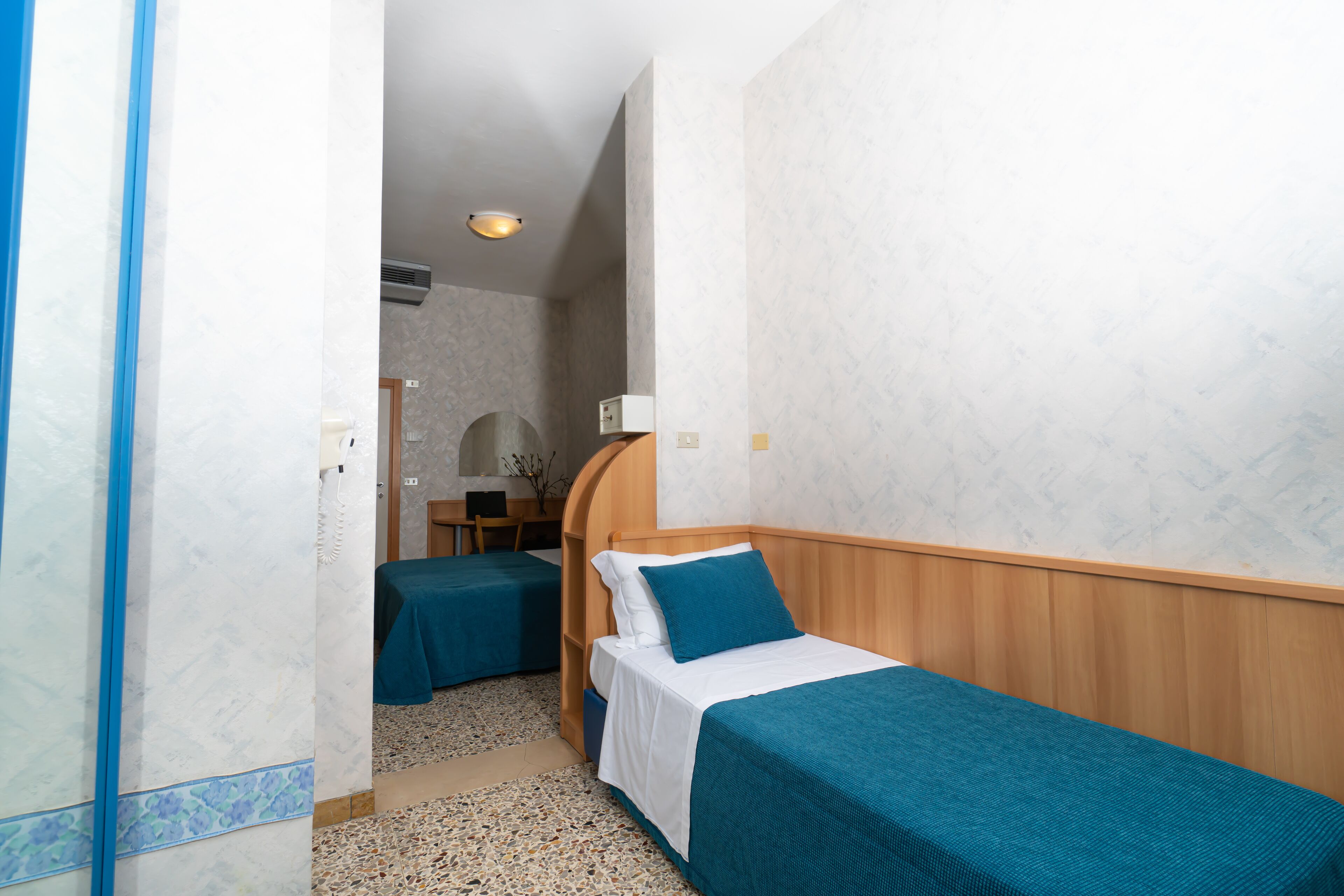 Ein Hotelzimmer mit zwei Einzelbetten, einem Holzkopfteil, einem kleinen Schreibtisch und einem Stuhl.