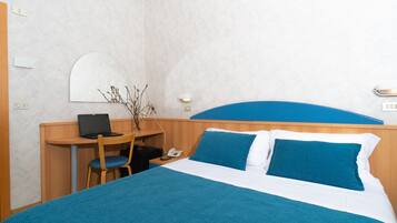 Quarto de hotel com cama, escrivaninha, cadeira, laptop e telefone.