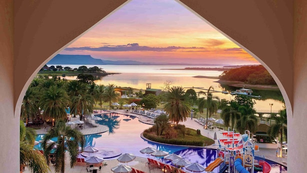 A resort pool area with a water slide, lounge chairs, and umbrellas. - Malai Manso Yacht Convention & Spa - All inclusive (Chapada dos Guimarães)