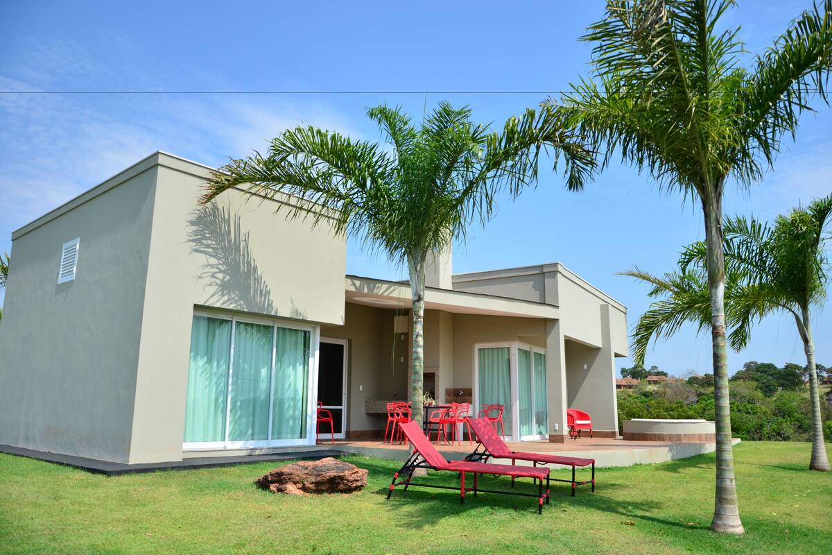 Una casa moderna de dos pisos con un patio, sillones reclinables rojos y una zona de barbacoa.