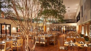A spacious indoor dining area with multiple tables and chairs, a central tree, and a balcony overlooking the dining space. - Malai Manso Yacht Convention & Spa - All inclusive (Chapada dos Guimarães)