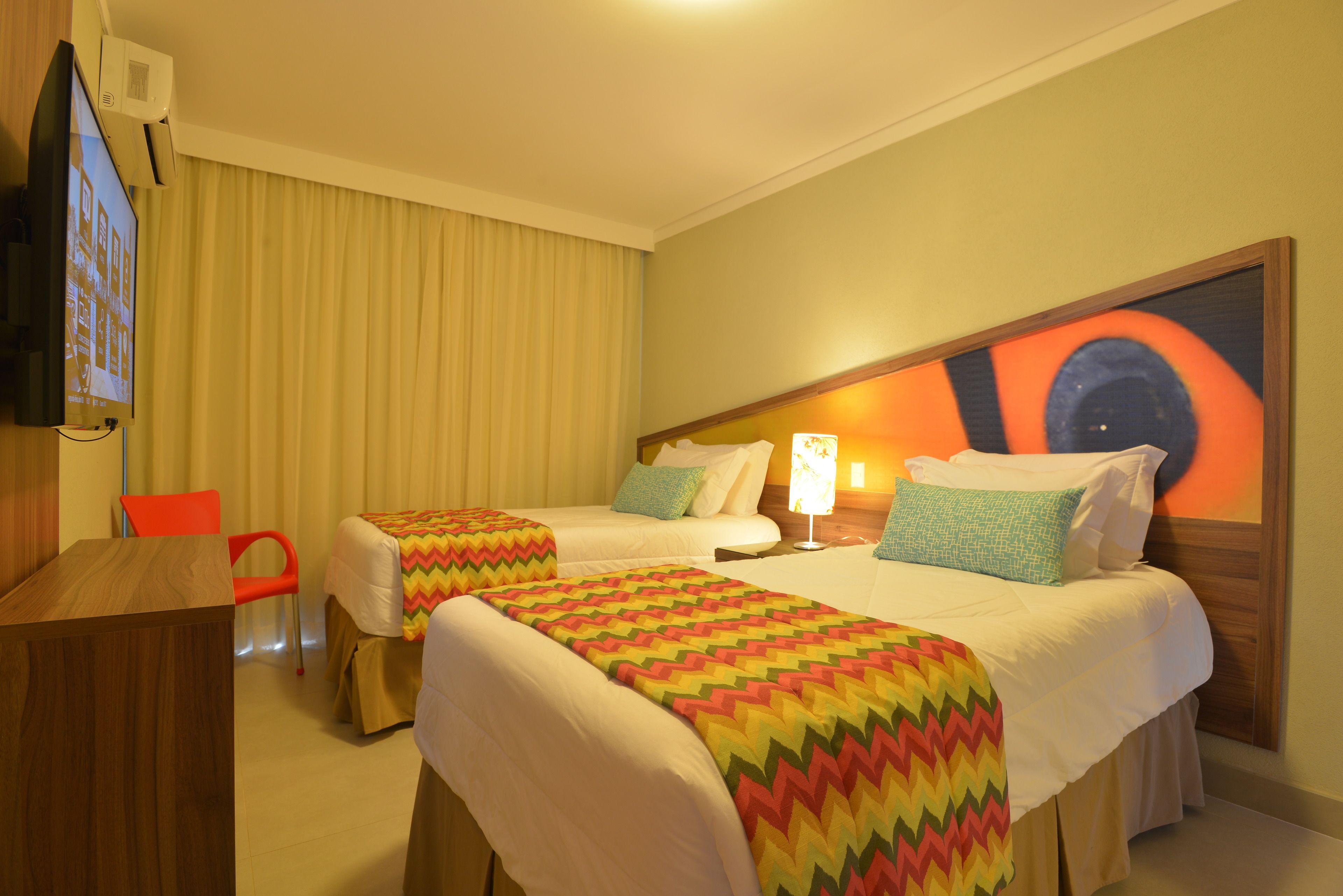A hotel room with two single beds, a TV, a desk, and a chair.