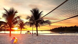 A beach volleyball net with palm trees and a sunset in the background. - Malai Manso Yacht Convention & Spa - All inclusive (Chapada dos Guimarães)