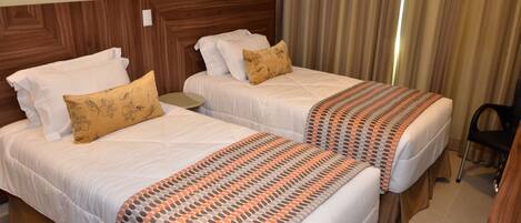 A hotel room with two beds, each with white bedding and patterned pillows. There is a small round table between the beds.