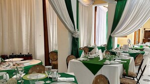 A dining area with tables set for a meal, featuring green tablecloths and white drapes. - PC ENTREPRISES Hotel (Port-au-Prince)
