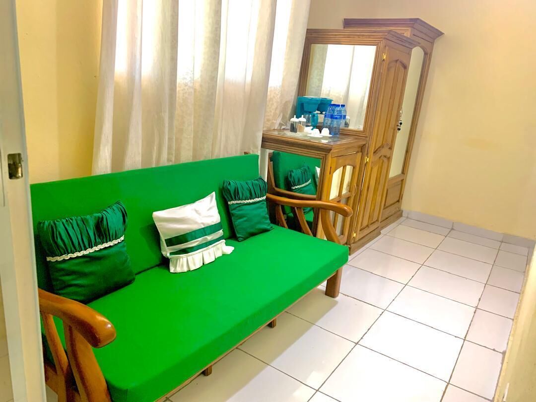 A green sofa with pillows, a wooden cabinet, and a tiled floor.