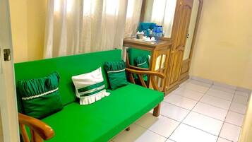 A green sofa with pillows, a wooden cabinet, and a tiled floor.