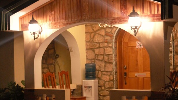 A small building with a stone facade, wooden door, and two lit lanterns. - PC ENTREPRISES Hotel (Port-au-Prince)