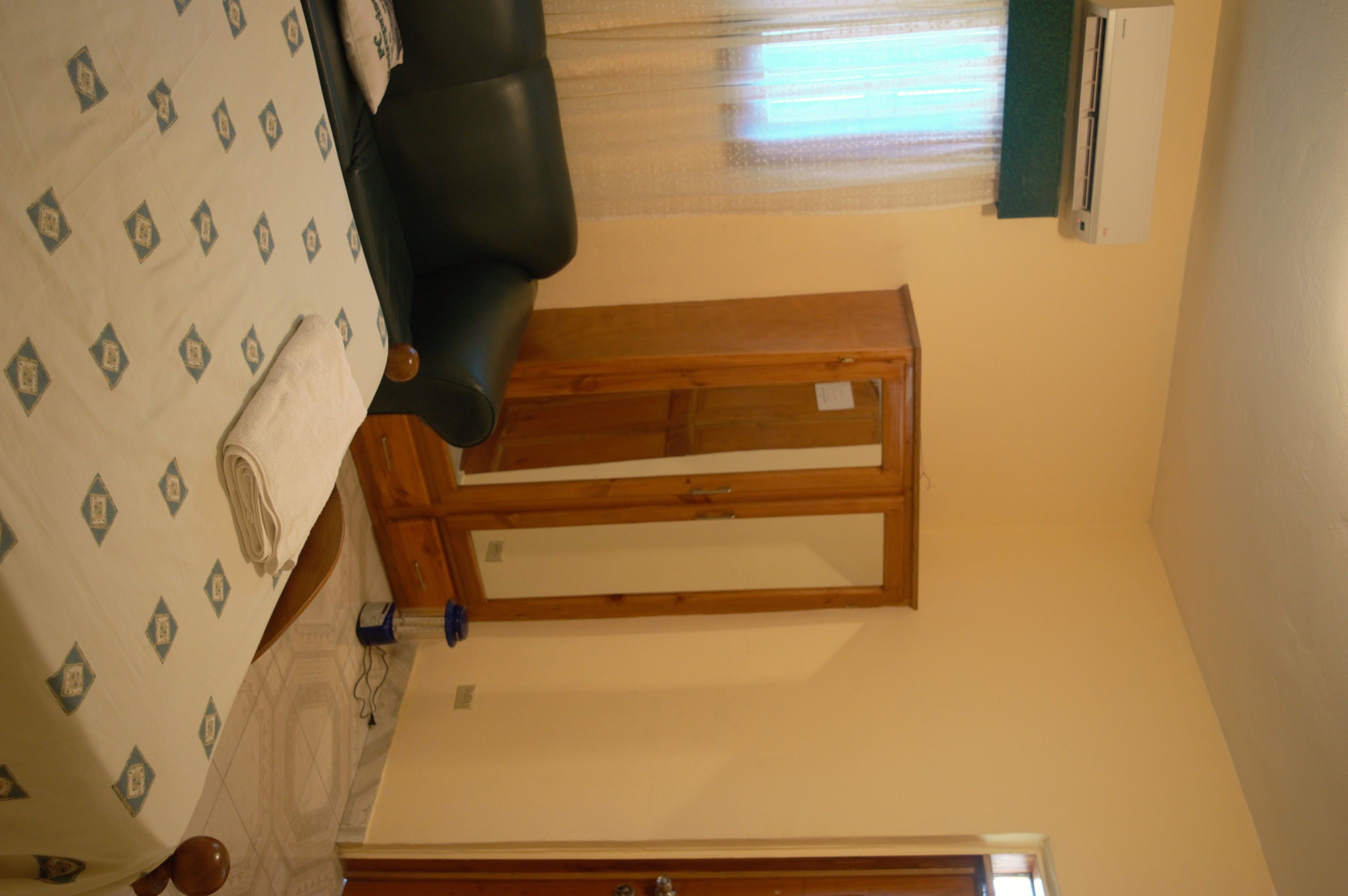 Una habitación con cama, cabecero de madera, ventana con persianas y aire acondicionado de pared.