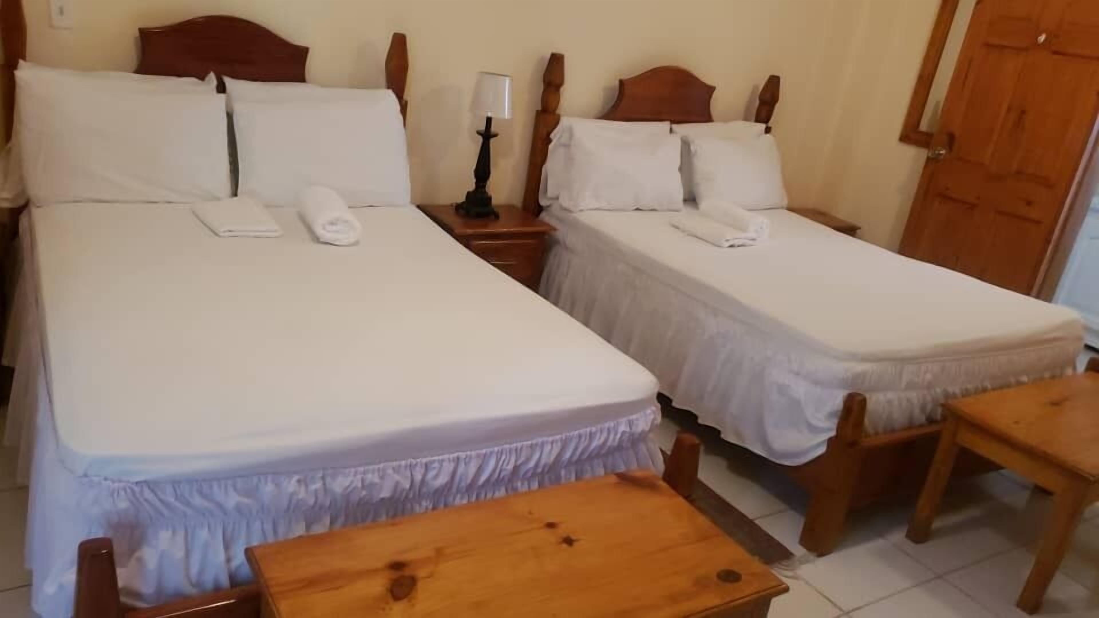 Quarto de hotel com duas camas de solteiro, mesa de cabeceira com abajur e uma mesa de madeira.
