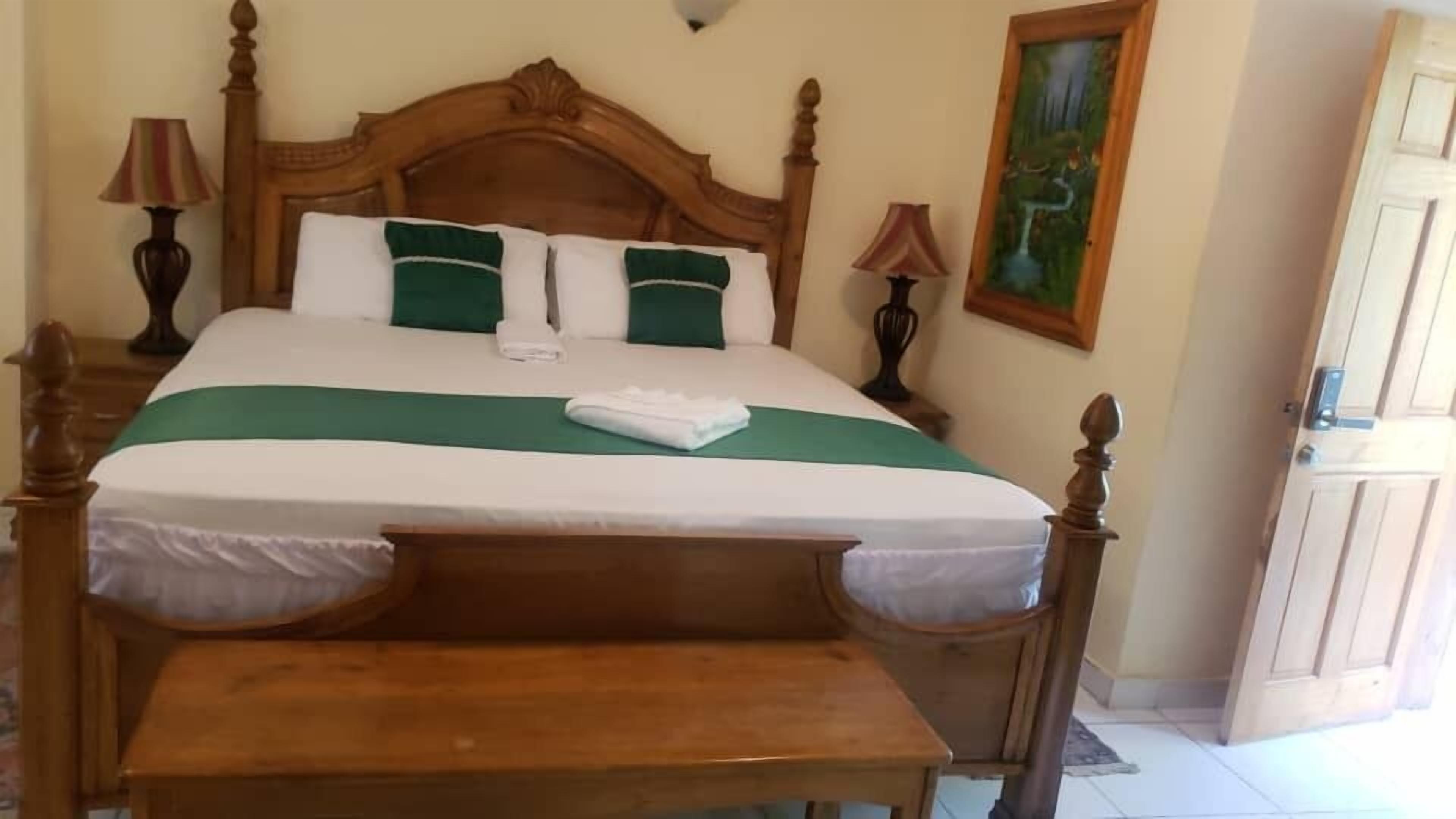 A neatly made bed with a wooden headboard, a green and white bedspread, and two pillows. There is a wooden bench at the foot of the bed.