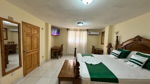A hotel room with a bed, a desk, a chair, a mirror, and a television. - PC ENTREPRISES Hotel (Port-au-Prince)