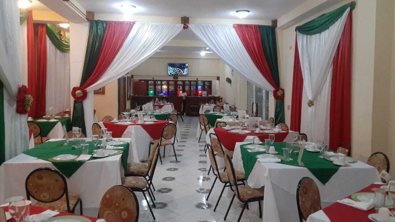 A restaurant with tables set for dining, draped curtains, and a television in the background.
