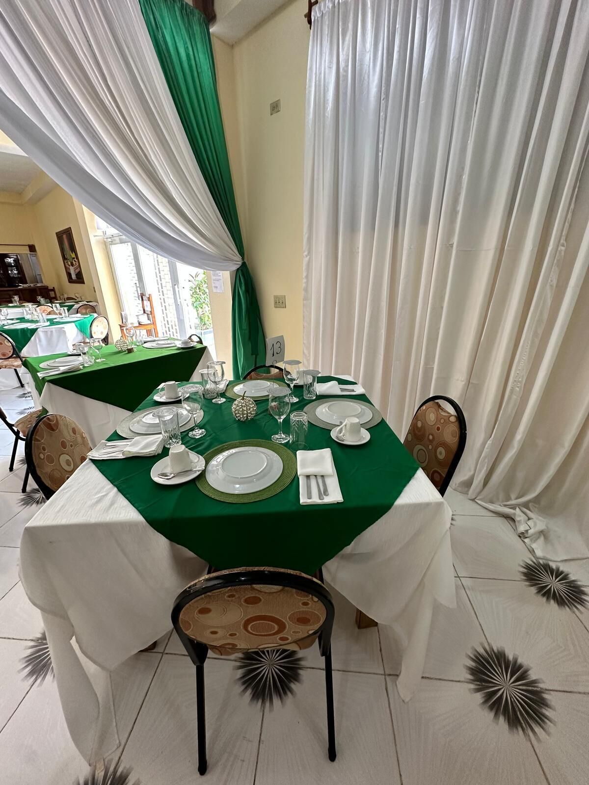 A dining area with a table set for four, featuring white and green tablecloths, plates, glasses, and cutlery.
