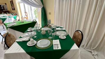A dining area with a table set for four, featuring white and green tablecloths, plates, glasses, and cutlery.