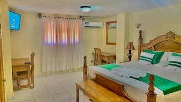 Una habitación de hotel con una cama de madera, un escritorio, una silla, un televisor y un aire acondicionado.