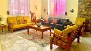 A living room with a yellow sofa, a wooden coffee table, and a stone accent wall. - PC ENTREPRISES Hotel (Port-au-Prince)