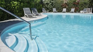 Ein Pool mit gewölbter Kante, umgeben von Liegestühlen und einem Metallgeländer.