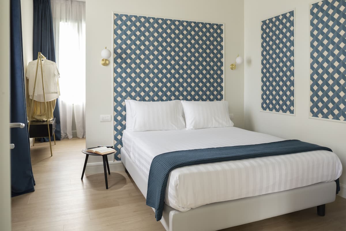 Un cuarto de hotel ordenado con una cama, una mesita de noche y una silla.