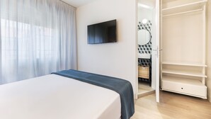 Ein Schlafzimmer mit einem Bett, einem an der Wand montierten Fernseher, einem offenen Kleiderschrank und einem durchgehenden Türrahmen einsehbaren Badezimmer.