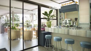 Eine moderne Bar mit einer Kaffeemaschine, Hockstühlen und einer großen Pflanze in einem Topf.
