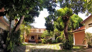 Un patio con un edificio central, rodeado de vegetación exuberante y plantas en macetas.