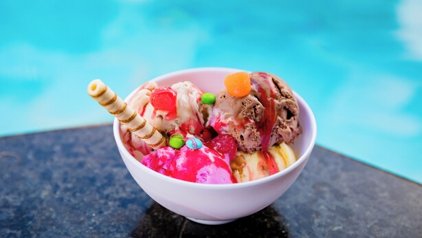A bowl of ice cream with various toppings, placed on a table near a pool. - Casa Blanca Park (Porto Seguro)