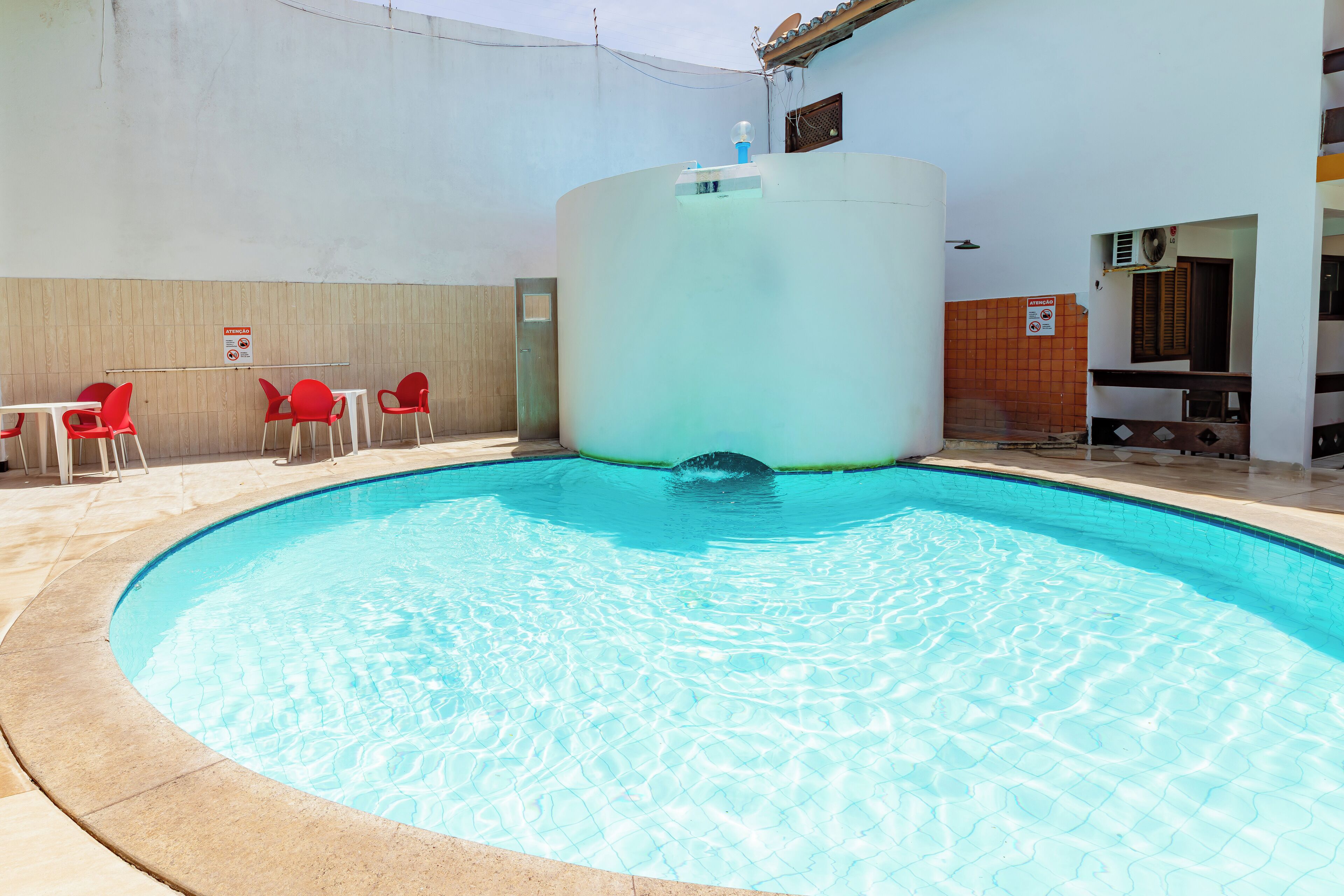 Una piscina dalla forma circolare, circondata da sedie rosse e un muro bianco.