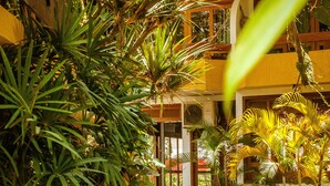 A pathway lined with tropical plants leading to a building with a tiled roof and wooden railings. - Casa Blanca Park (Porto Seguro)