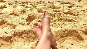 A pair of feet resting on a sandy beach with the ocean in the background. - Casa Blanca Park (Porto Seguro)