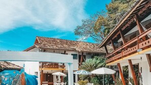A swimming pool with dolphin and fish sculptures, surrounded by outdoor seating and a building with a tiled roof. - Casa Blanca Park (Porto Seguro)