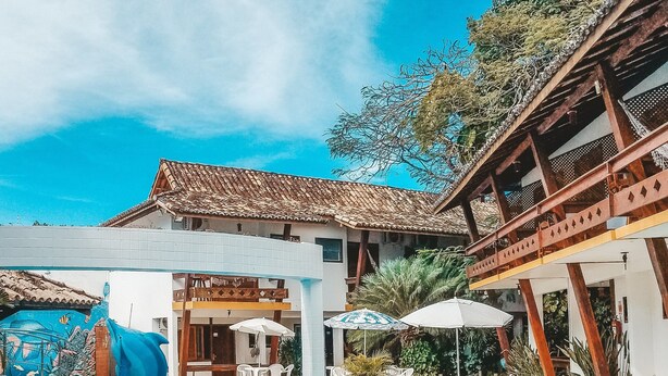 A swimming pool with dolphin and fish sculptures, surrounded by outdoor seating and a building with a tiled roof. - Casa Blanca Park (Porto Seguro)