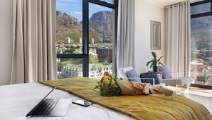 A hotel room with a bed, a laptop, a bouquet of flowers, and a view of a cityscape and mountains.