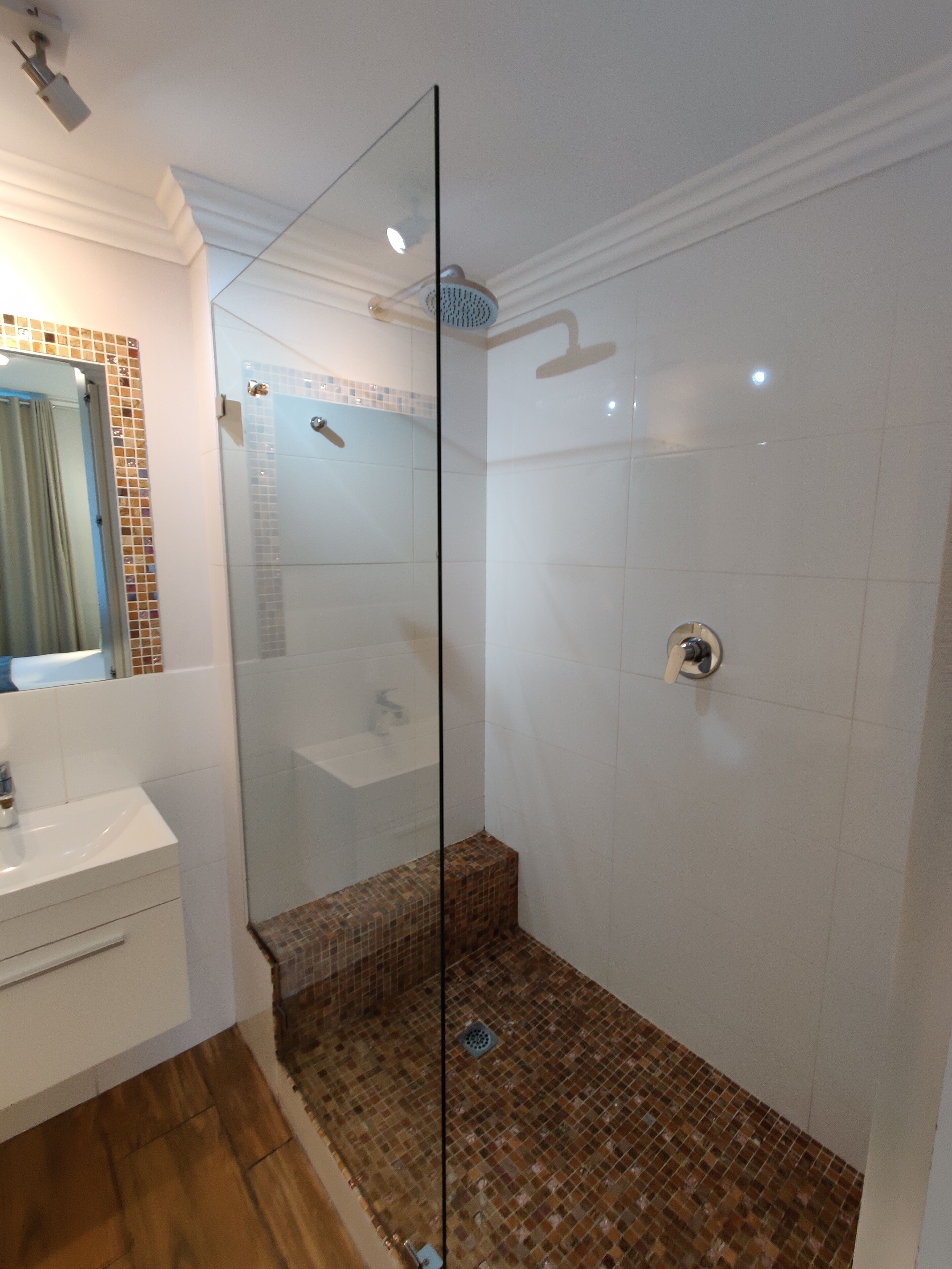 A modern bathroom with a glass shower enclosure, a white sink, and a tiled floor.