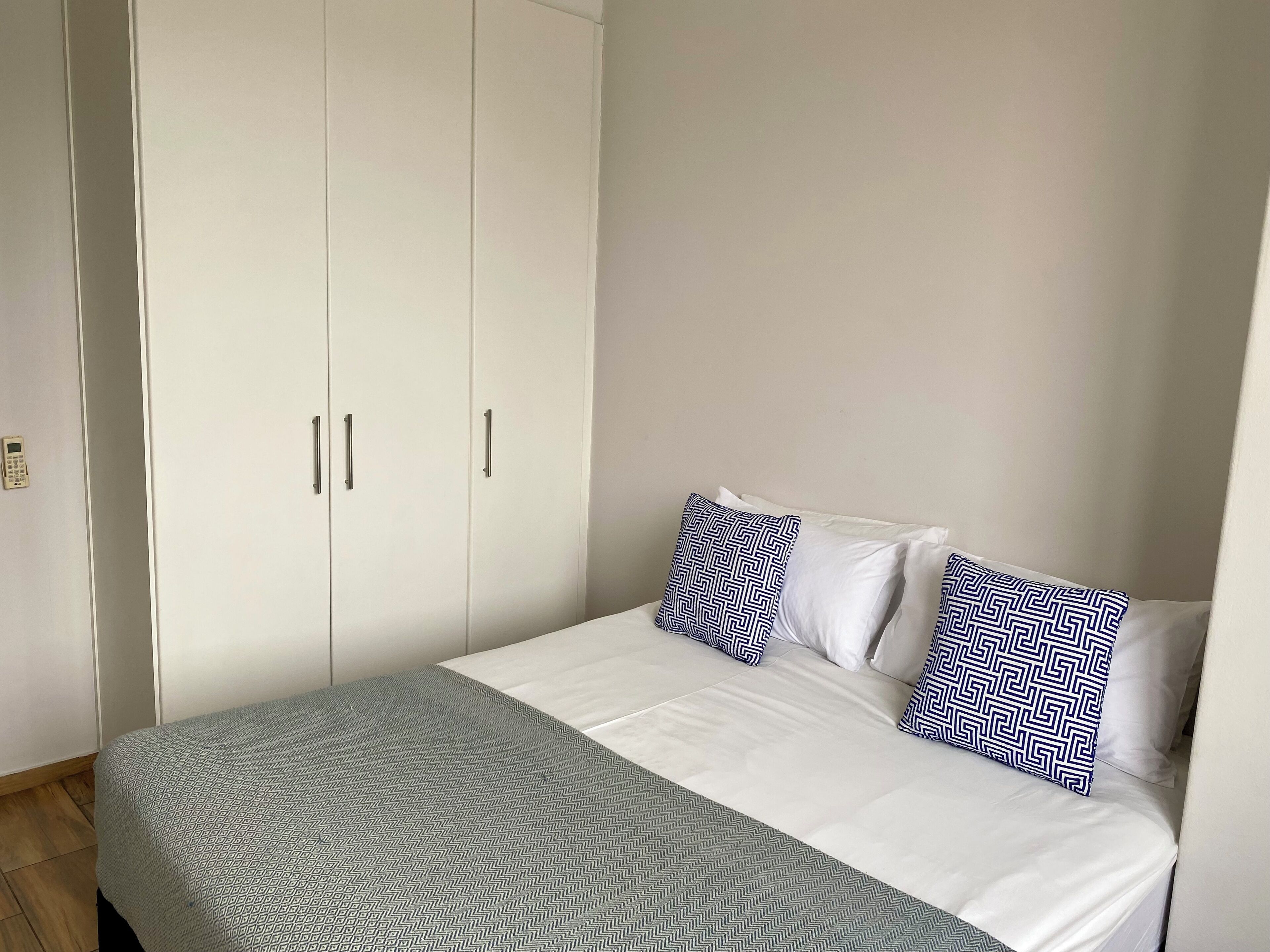 A bedroom with a bed, white wardrobe, and patterned pillows.