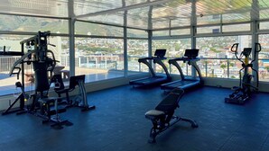A gym with treadmills, a bench, and weight machines, featuring large windows with a city view. - Urban Oasis at Perspectives (Cape Town)