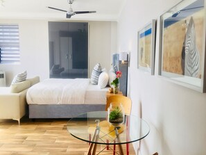 A modern bedroom with a bed, a glass table, a wardrobe, and a ceiling fan. - Urban Oasis at The Square (Cape Town)