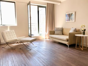 A modern living room with a white sofa, a white chair, a small round table, and a large window with curtains. - Urban Oasis at The Square (Cape Town)