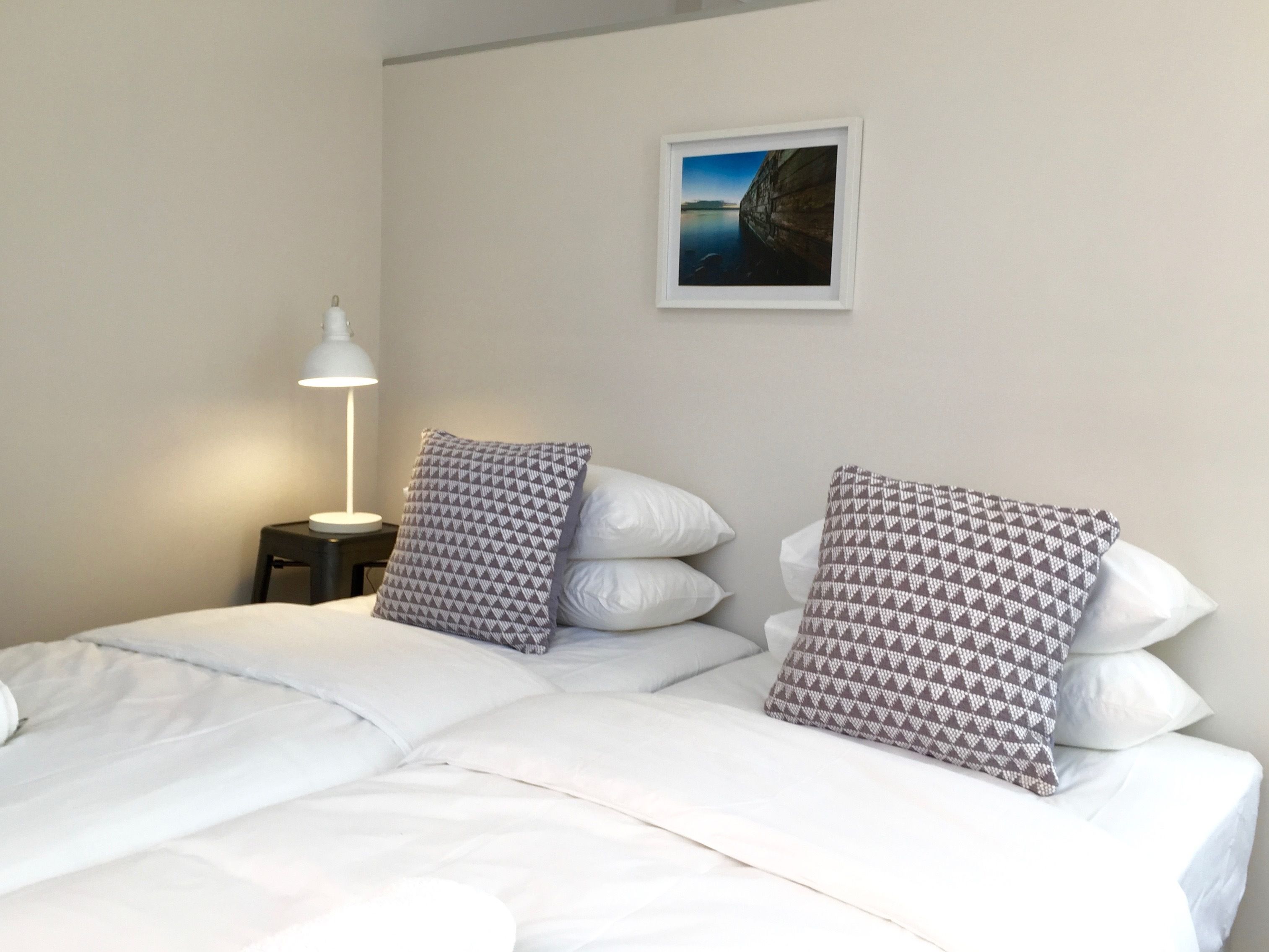 A neatly made bed with white linens and patterned pillows, a bedside lamp, and a framed picture on the wall.