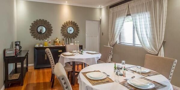 A dining area with round tables set for four, a coffee station, and decorative mirrors on the wall. - Bhotani Bed and Breakfast (Gqeberha (Port Elizabeth))