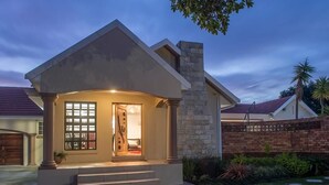 A modern house with a stone chimney, a well-lit entrance, and a brick pathway leading to the door. - Bhotani Bed and Breakfast (Gqeberha (Port Elizabeth))