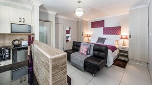 A modern apartment with a kitchen, a living area with a sofa and a bed, and a dining area. - Bhotani Bed and Breakfast (Gqeberha (Port Elizabeth))