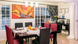 A dining area with a table set for four, chairs with red and black upholstery, a painting on the wall, and a window with curtains. - Bhotani Bed and Breakfast (Gqeberha (Port Elizabeth))